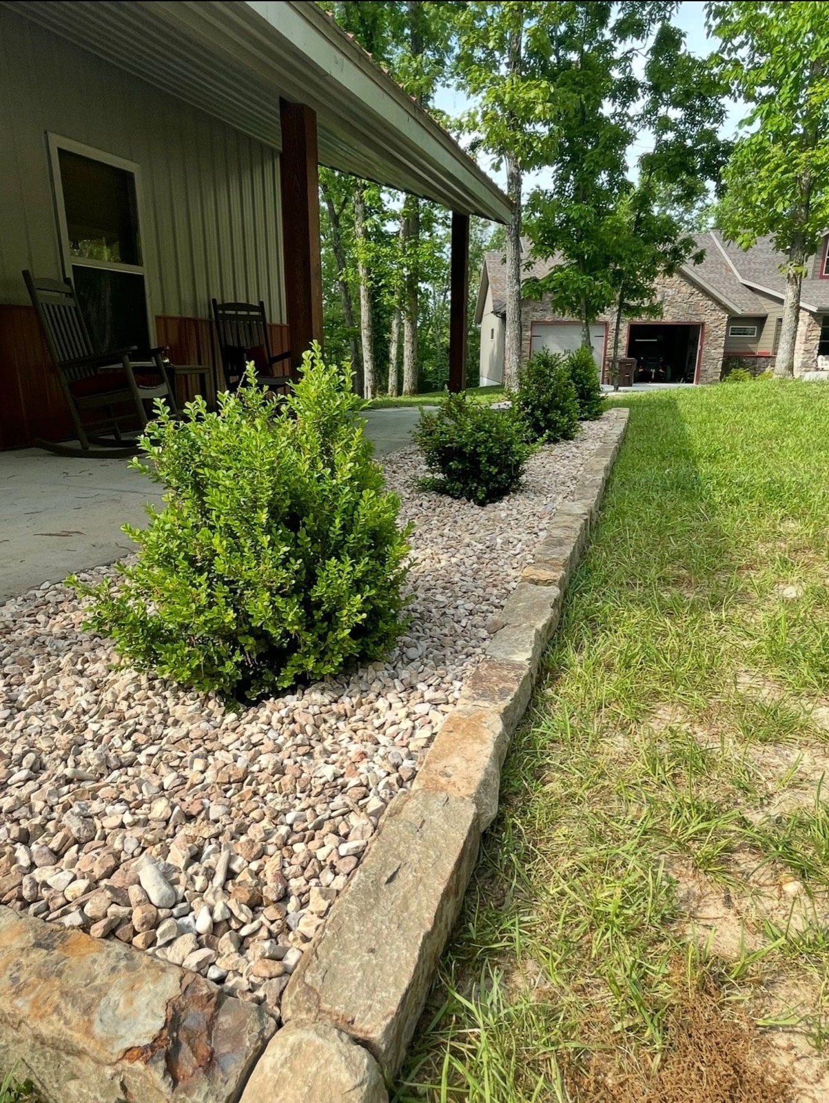 Stone-edged gravel beds with fresh boxwood plantings along a covered porch