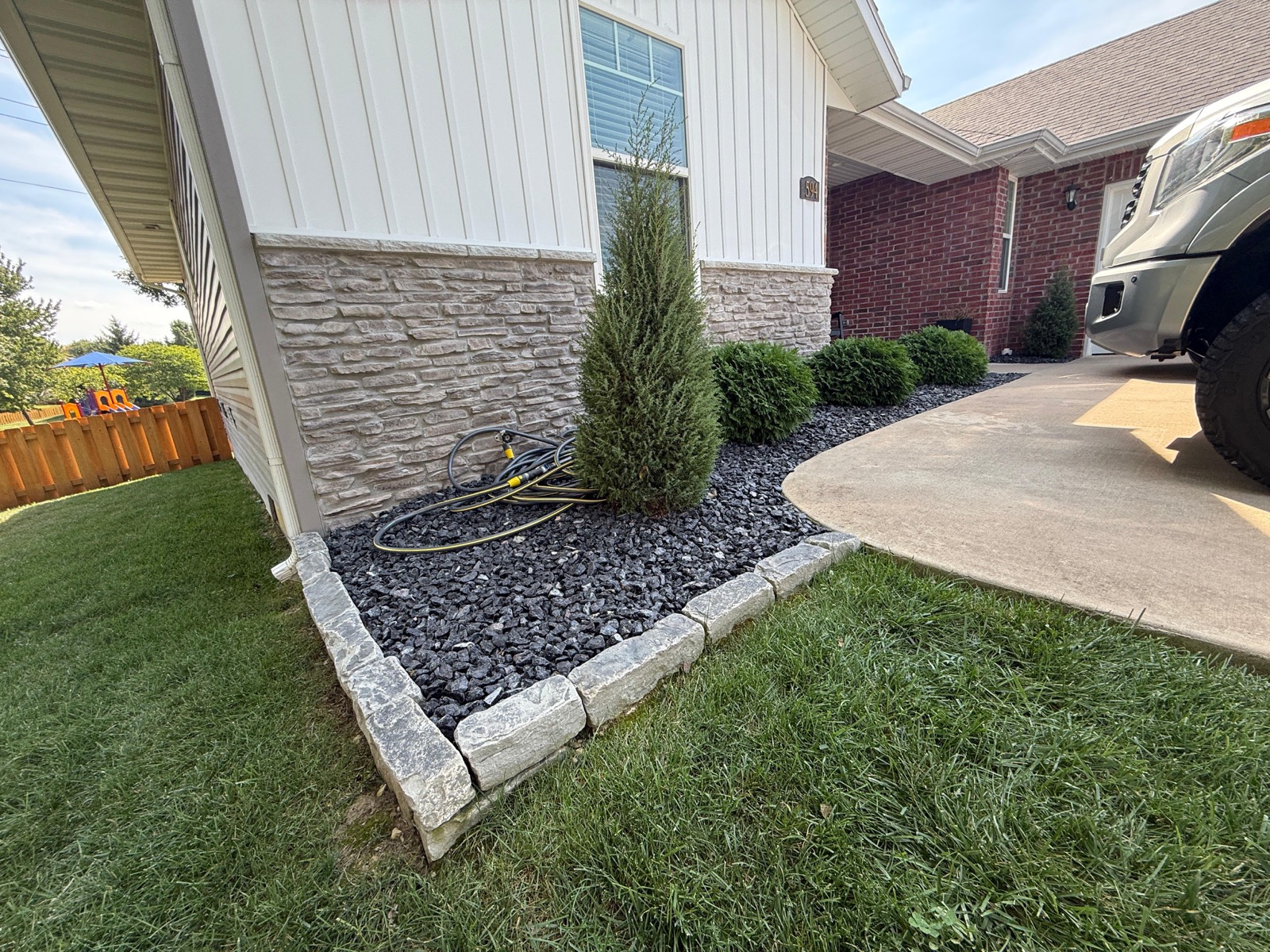 Black gravel bed with stone block edging and a new evergreen
