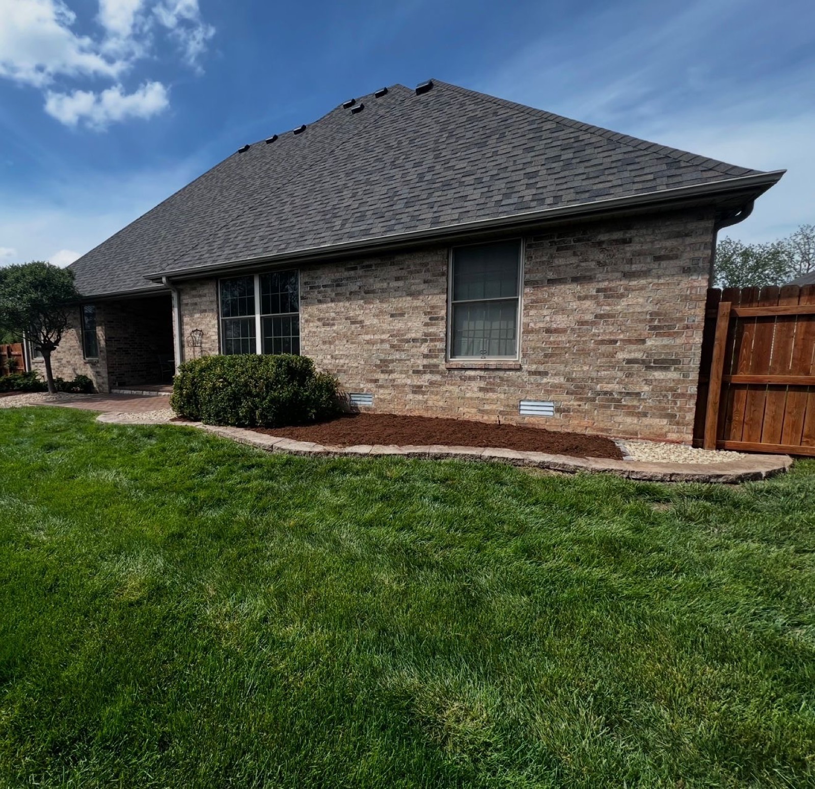 Fresh mulch bed wrapping a brick home with a striped lawn
